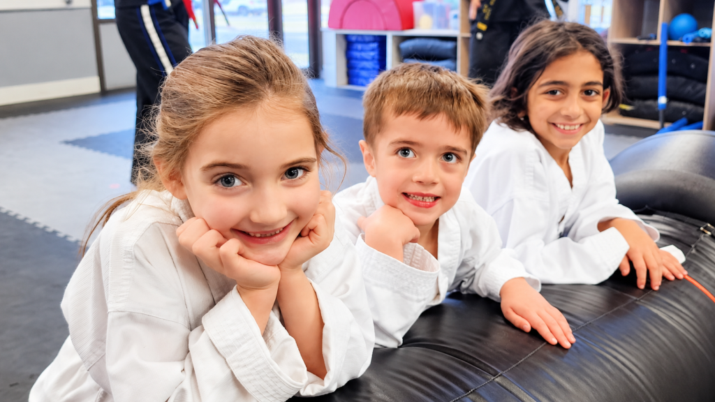 Three smiling Taekwondo students leaning on a training bag at DK Fitness Arts.